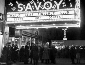 1938. Un gruppo di persone sotto l'insegna del Savoy ad Harlem che annuncia la gara di Lindy Hop